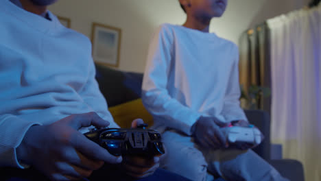 Nahaufnahme-Der-Hände-Von-Zwei-Kleinen-Jungen-Zu-Hause,-Die-Spät-In-Der-Nacht-Mit-Einer-Computerspielkonsole-Im-Fernsehen-Spielen-Und-Controller-Halten-7